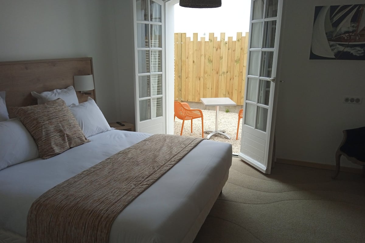 A bedroom with a large bed, a wooden headboard, and a view of an outdoor area with a table and chairs.