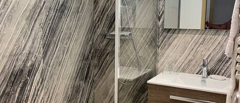 A modern bathroom with a glass-enclosed shower, marble walls, a wooden vanity, and a mirror above the sink.