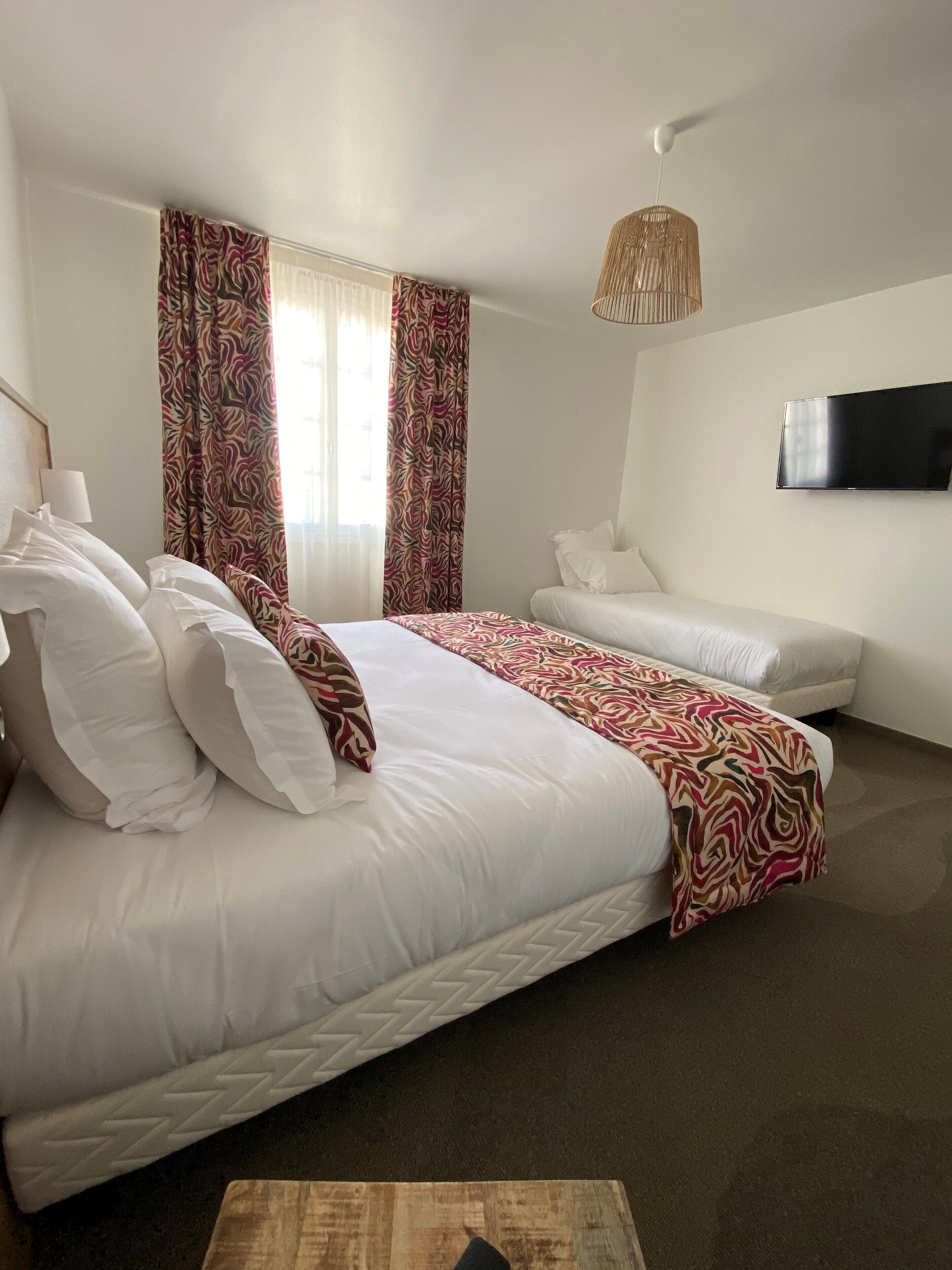 A hotel room with a large bed, a sofa, a television, and a patterned curtain.