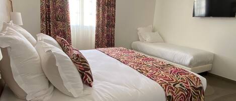 A hotel room with a large bed, a sofa, a television, and a patterned curtain.