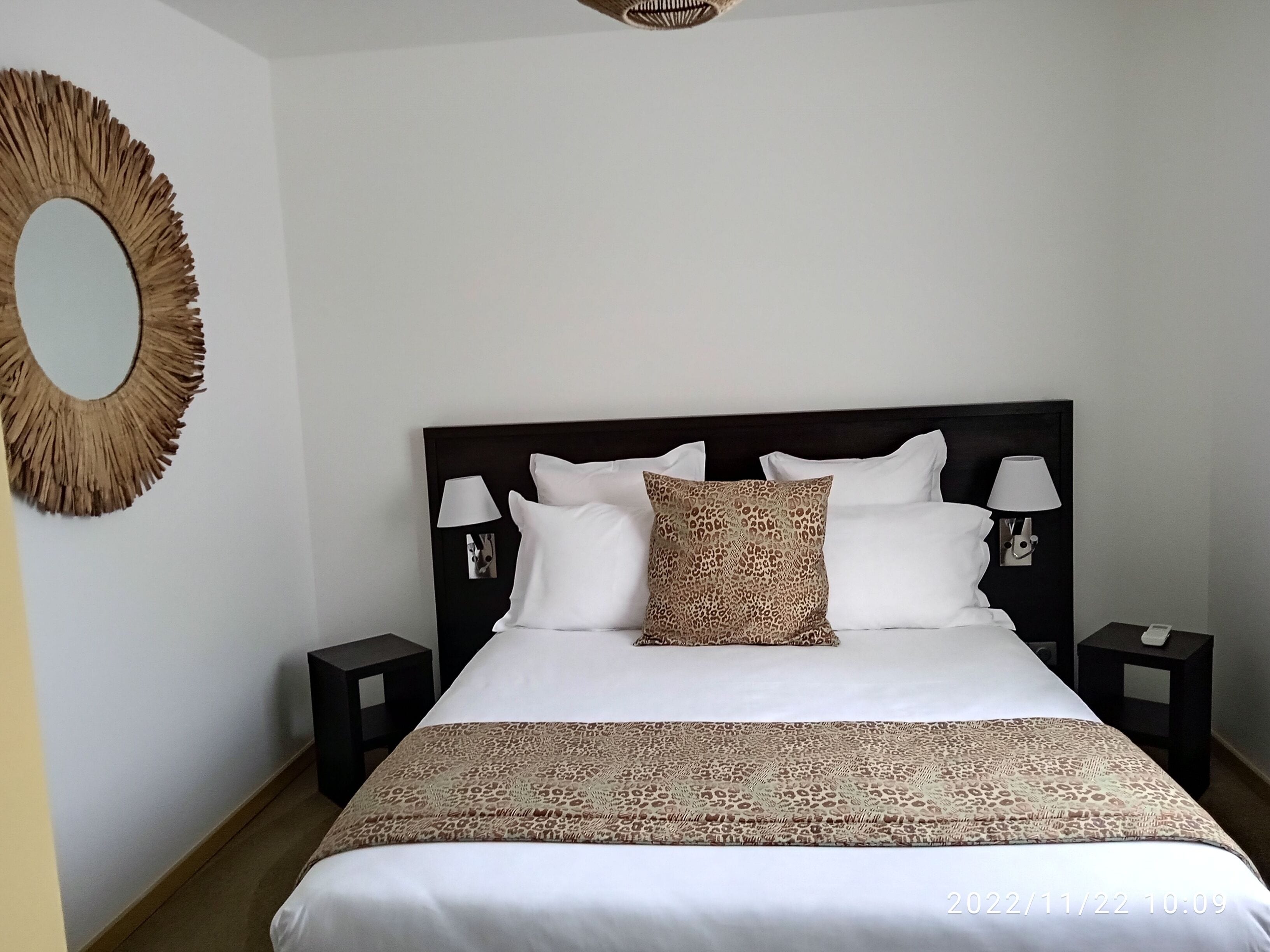 A neatly made bed with a patterned bedspread, two bedside lamps, and a decorative mirror on the wall.