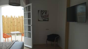 Una habitación con cama, televisión, puerta que da a un balcón, una silla y una mesita.