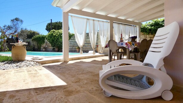 A covered outdoor area with a pool, lounge chairs, and a table with a floral tablecloth. - La Vigna Salentina - Garden and Private Pool (Alessano)