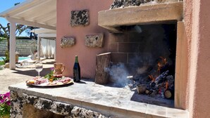 An outdoor grill area with a stone wall, a hanging chair, and a table with food and drinks. - La Vigna Salentina - Garden and Private Pool (Alessano)