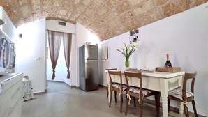 A kitchen with a dining table, chairs, a refrigerator, and a vase with flowers. - La Vigna Salentina - Garden and Private Pool (Alessano)