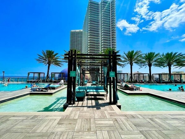A resort pool area with multiple swimming pools, lounge chairs, and palm trees.