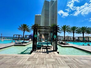 A rooftop pool area with multiple swimming pools, lounge chairs, and palm trees. - Amazing Views at a Complete Resort BY rent4us (Hollywood)