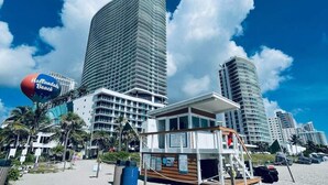 Un hotel frente a la playa con vistas al mar, palmeras y un puesto de salvavidas.