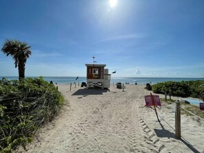 Une tour de surveillance, où se tient un sauveteur, sur une plage de sable fin, sous un ciel dégagé.