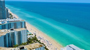 A coastal hotel with multiple high-rise buildings, a beach with umbrellas, and a clear view of the ocean.