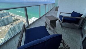 A balcony with wicker furniture and a view of the ocean and buildings.