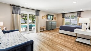 A hotel room with a bed, a sofa, a TV, a dresser, and a pool view.
