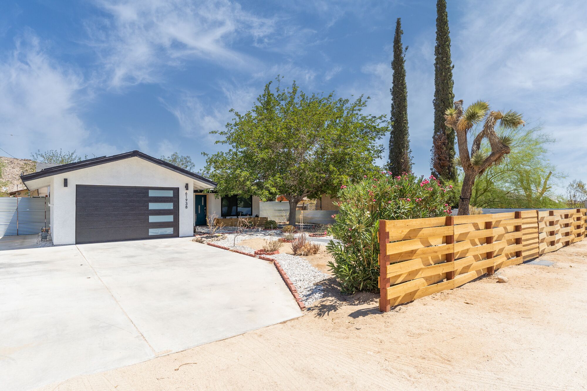 A modern house with a garage, a covered patio, and a landscaped garden with cacti and trees.