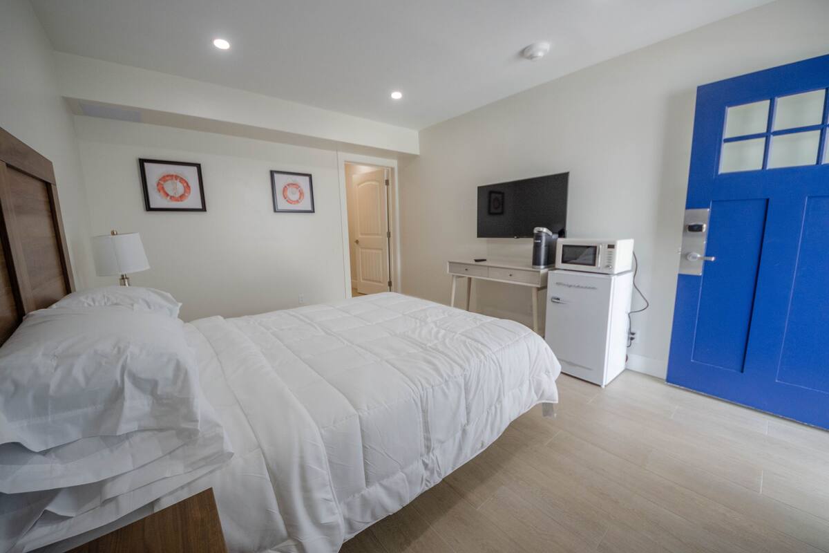 A hotel room with a bed, a desk with a microwave, a TV, and a blue door.