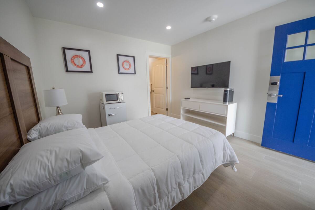 A bedroom with a bed, a desk, a microwave, and a blue door.