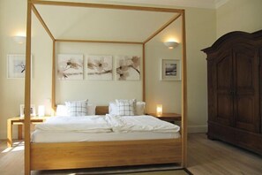 A four-poster bed with a wooden frame, a white mattress, and two bedside tables with lamps. There are three framed artworks on the wall above the bed. - Gutshaus Zicker in Garz (Garz)