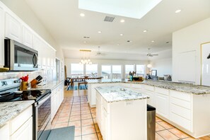 A spacious kitchen with white cabinetry, a large island, and a view to the outside. - Beachfront Home w/ Pavilion, Private Walkover & Updated Interior! (Galveston)