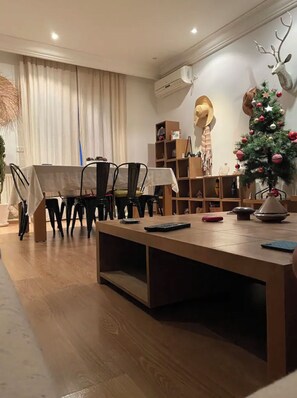 A modern living room with a wooden dining table, chairs, a sofa, and a Christmas tree.