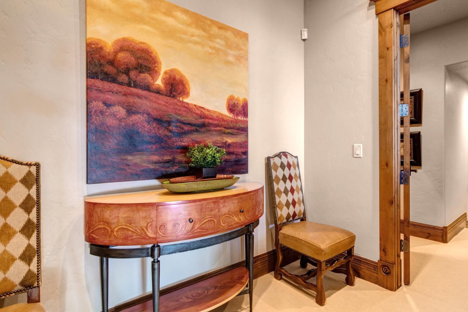 Un pasillo con una silla de madera, una consola con una planta y un cuadro en la pared.