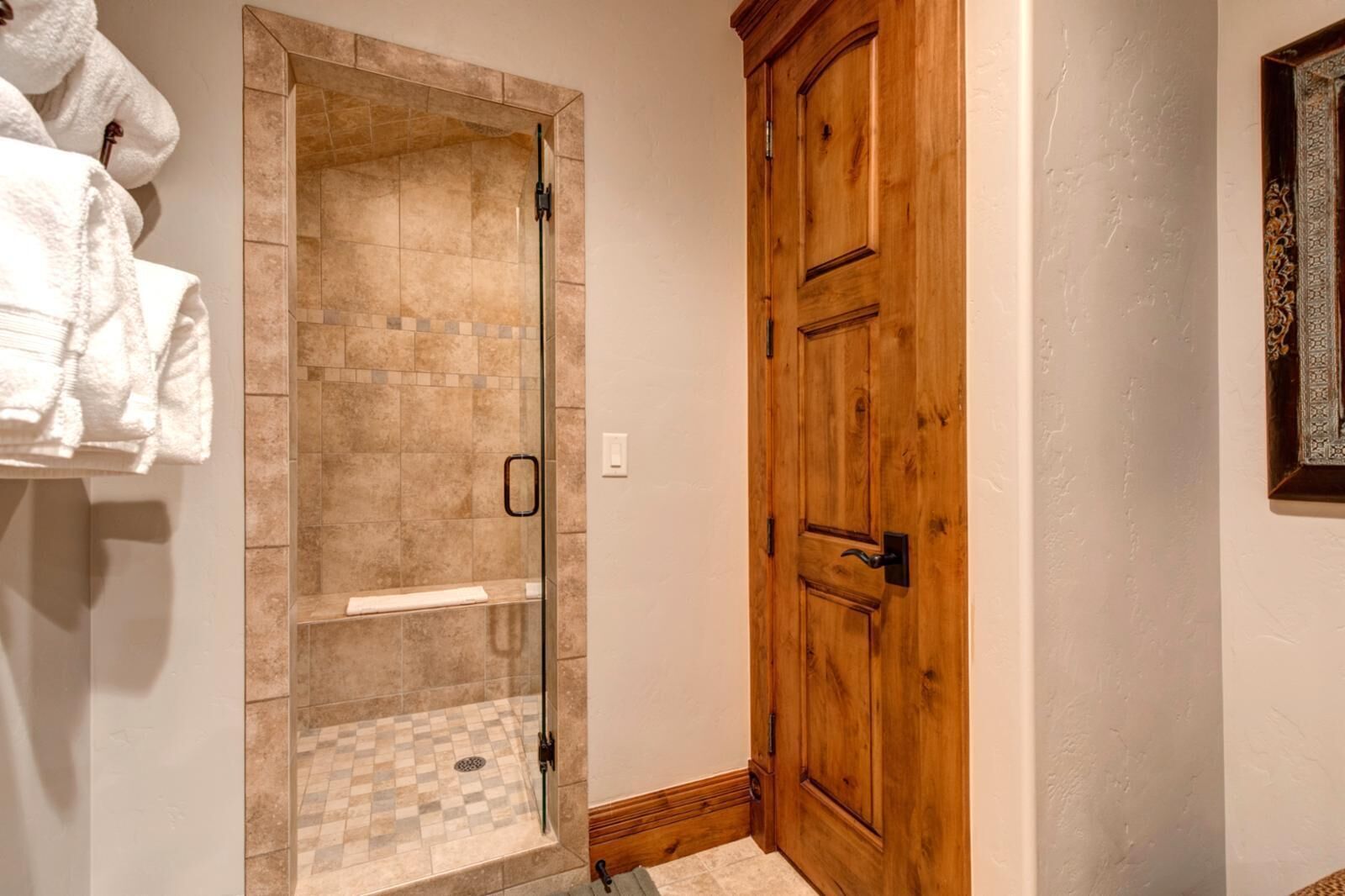 A bathroom with a glass-enclosed shower, a wooden door, and a towel rack with towels.