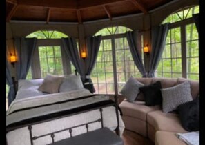 A bedroom with a bed, a sofa, and large windows with curtains.
