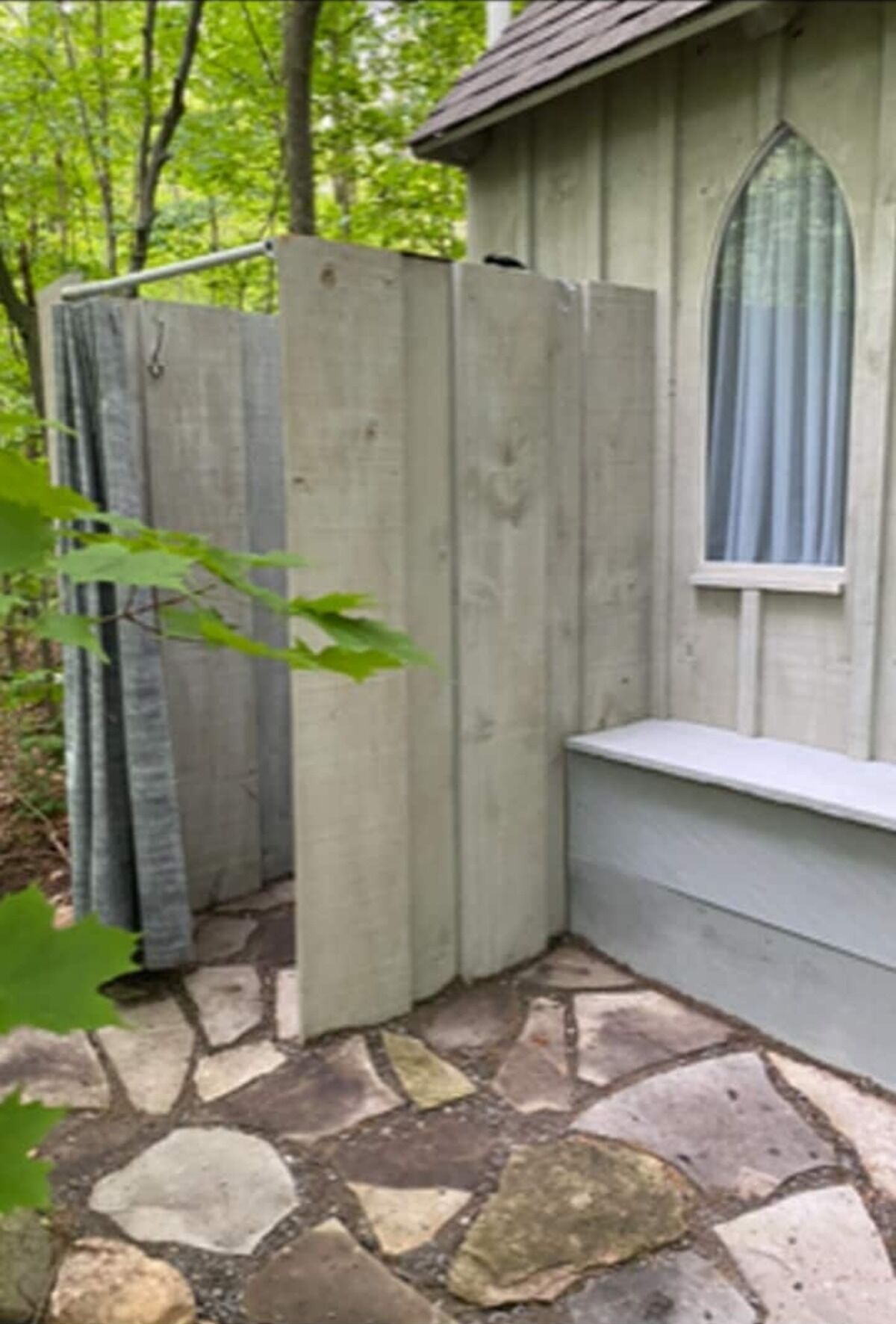 A stone-tiled patio with a wooden fence and a window with a curtain.
