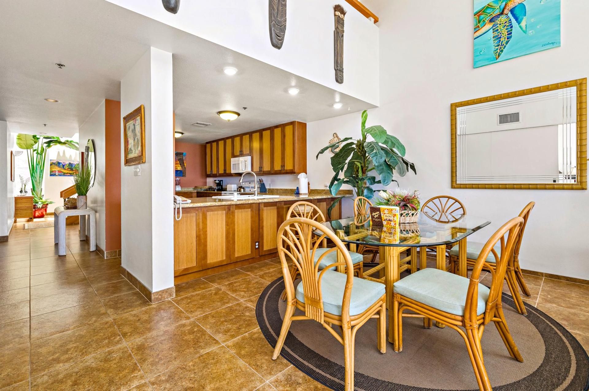 A dining area with a glass table, wicker chairs, and a large plant.