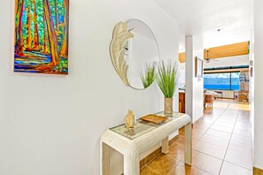 A hallway with a glass-top console table, a large mirror, and a colorful painting. - Sands of Kahana | Ocean View 3 BR | Car Incl. w/ 6+ Nights | SOK-292 by KBM (Lahaina)