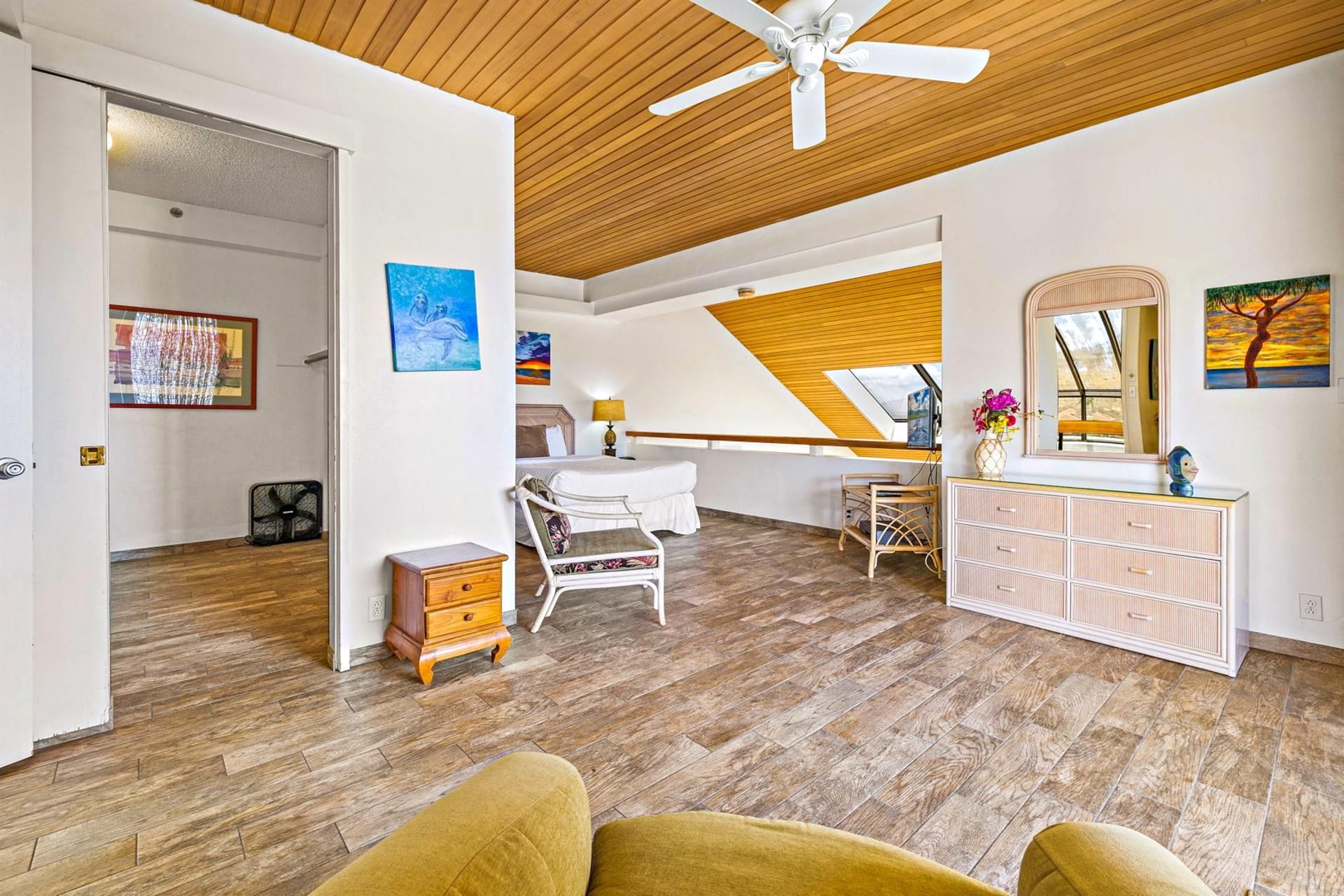 A spacious room with a sloped ceiling, a bed, a dresser, and a chair.