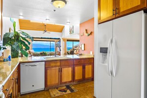 A kitchen with a view of the ocean, wooden cabinets, a white refrigerator, and a ceiling fan. - Sands of Kahana | Ocean View 3 BR | Car Incl. w/ 6+ Nights | SOK-292 by KBM (Lahaina)