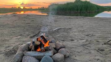 A campfire on a sandy beach with a sunset in the background.