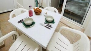 A small, white dining table with two chairs, a bowl, a cup, and a spoon set on a tiled floor. - Appât T2 en Rdc à 50 Mètres de la Plage (Saint Palais sur Mer)
