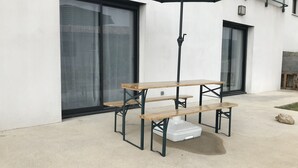 Een picknicktafel met een zwarte parasol, voor een modern gebouw met grote glazen deuren.
