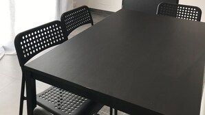Een kamer met een grote zwarte tafel en vier zwarte stoelen. Er is een deur en een raam met zonwering.