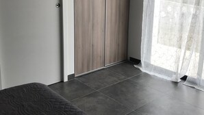 Een slaapkamer met een bed, een kledingkast en een raam met dunne gordijnen.