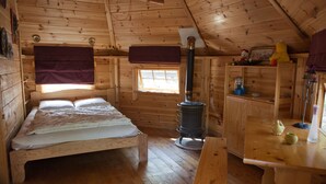 A wooden cabin with a bed, a table, a window, and a wood stove. - Cabane : île aux Canets, Thoureil, Maine & Loire (Gennes-Val-de-Loire)