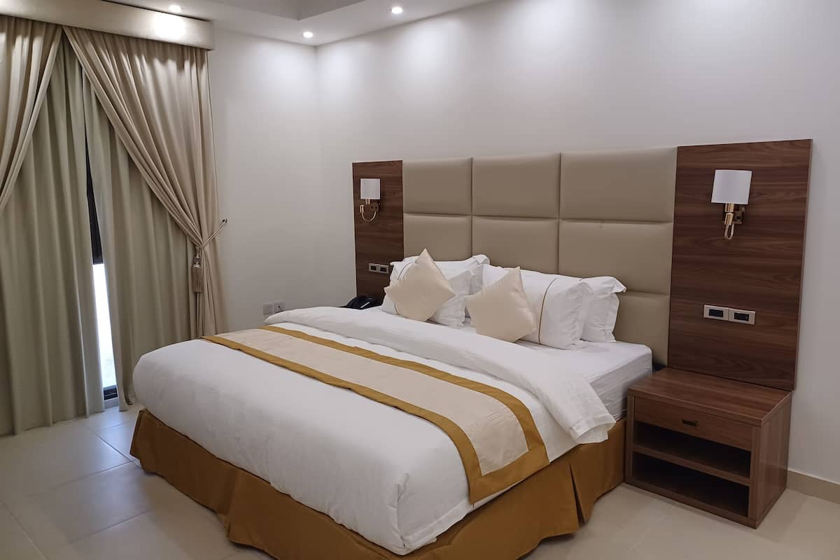 A modern hotel room with a large bed, beige curtains, and a wooden headboard.
