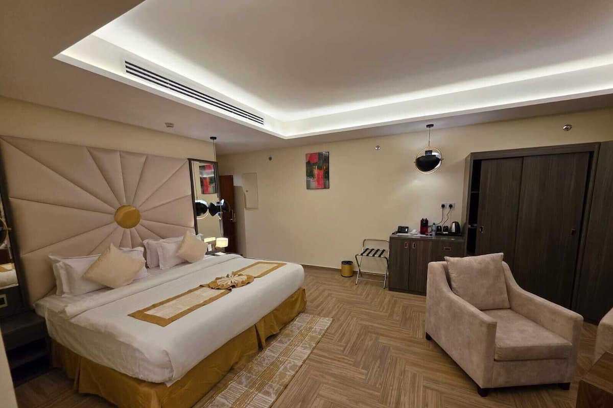A modern hotel room with a large bed, a sitting area, and a wardrobe.