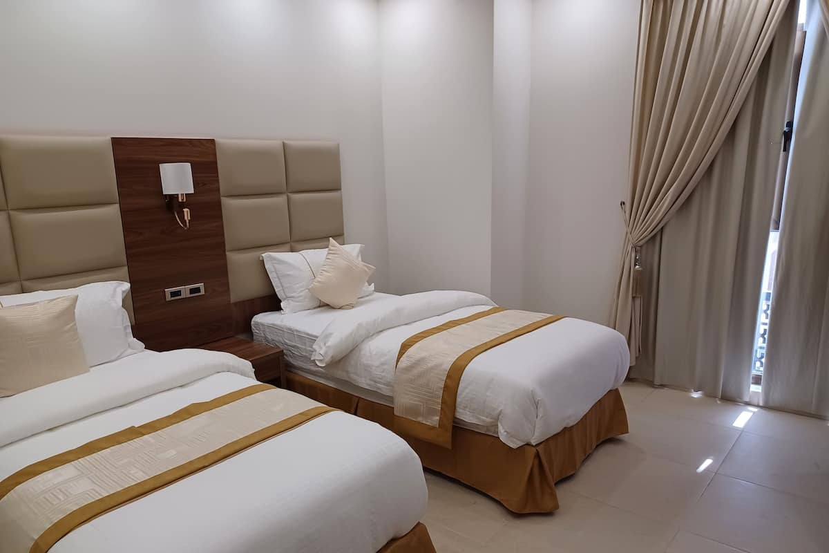 A hotel room with two beds, a wooden headboard, a nightstand, and a window with curtains.
