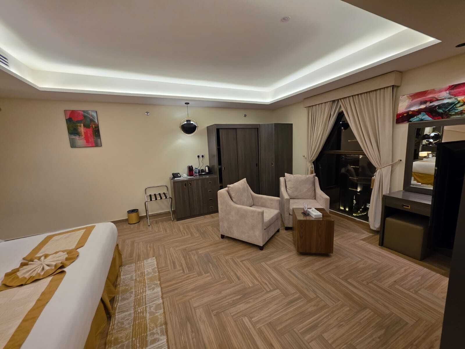 Una habitación de hotel moderna con una cama, dos sillones, una mesita, un armario y un televisor.