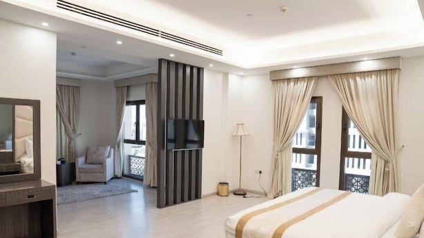 Quarto de hotel moderno com uma cama grande, televisão, escrivaninha e varanda com cortinas.