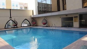 Uma piscina interior com água cristalina, rodeada por um deck revestido de azulejos. Há duas cadeiras suspensas com almofadas vermelhas.