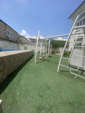 Un área de juegos al aire libre con césped artificial, una estructura de escalada y un muro de piedra.