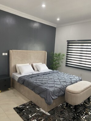 Un dormitorio moderno con cama, mesitas de noche, un banco, una planta y una ventana con persianas.