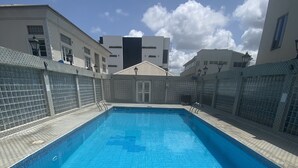 Une piscine rectangulaire à l’eau d’un bleu limpide, entourée d’une terrasse carrelée et d’une petite clôture.