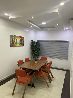 Un salón de conferencias con una mesa de madera y sillas naranjas, una planta en maceta y un cuadro en la pared.