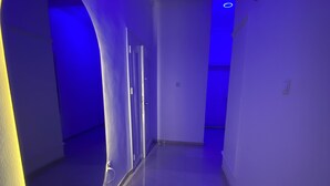 Un couloir avec un miroir incurvé sur le côté gauche, une porte sur le côté droit et un spot encastré au plafond.