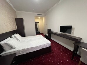Comfortable room with a neatly made bed, flat-screen TV, and mirror.