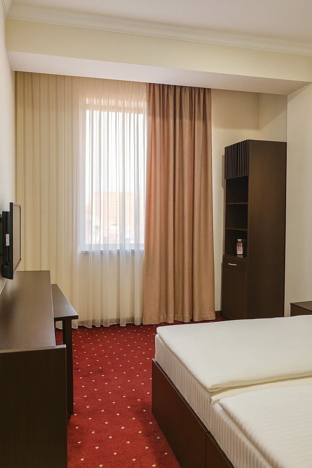 A hotel room with a bed, a desk, a wardrobe, and a window with curtains.
