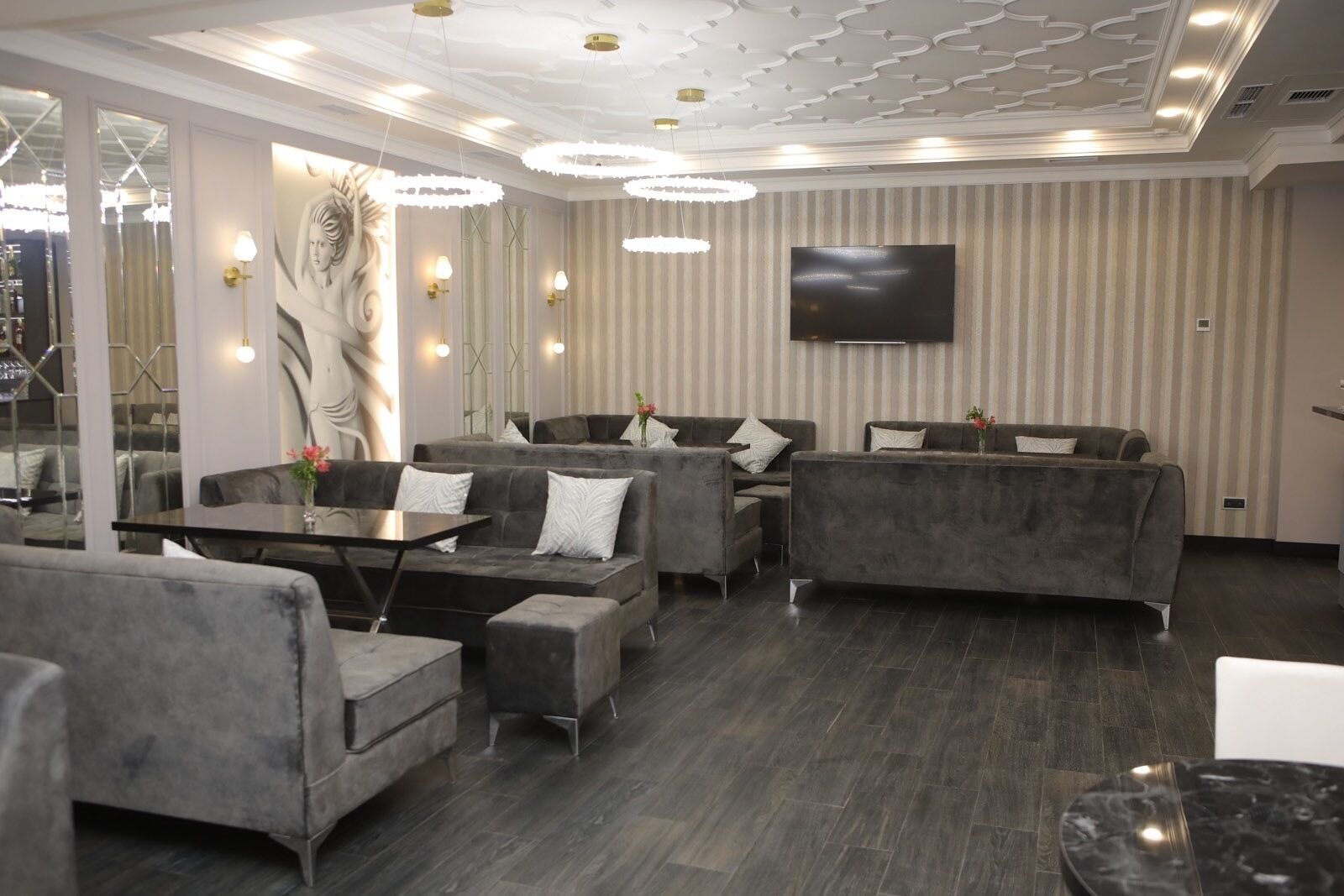 Zona relax moderna con divani grigi, un televisore a schermo piatto e una parete decorata.